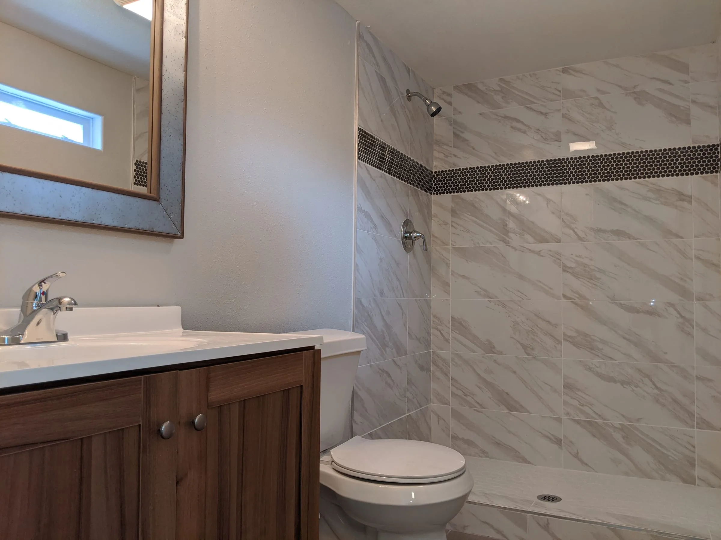Renovated bathroom with marble-look shower tile and a wood vanity