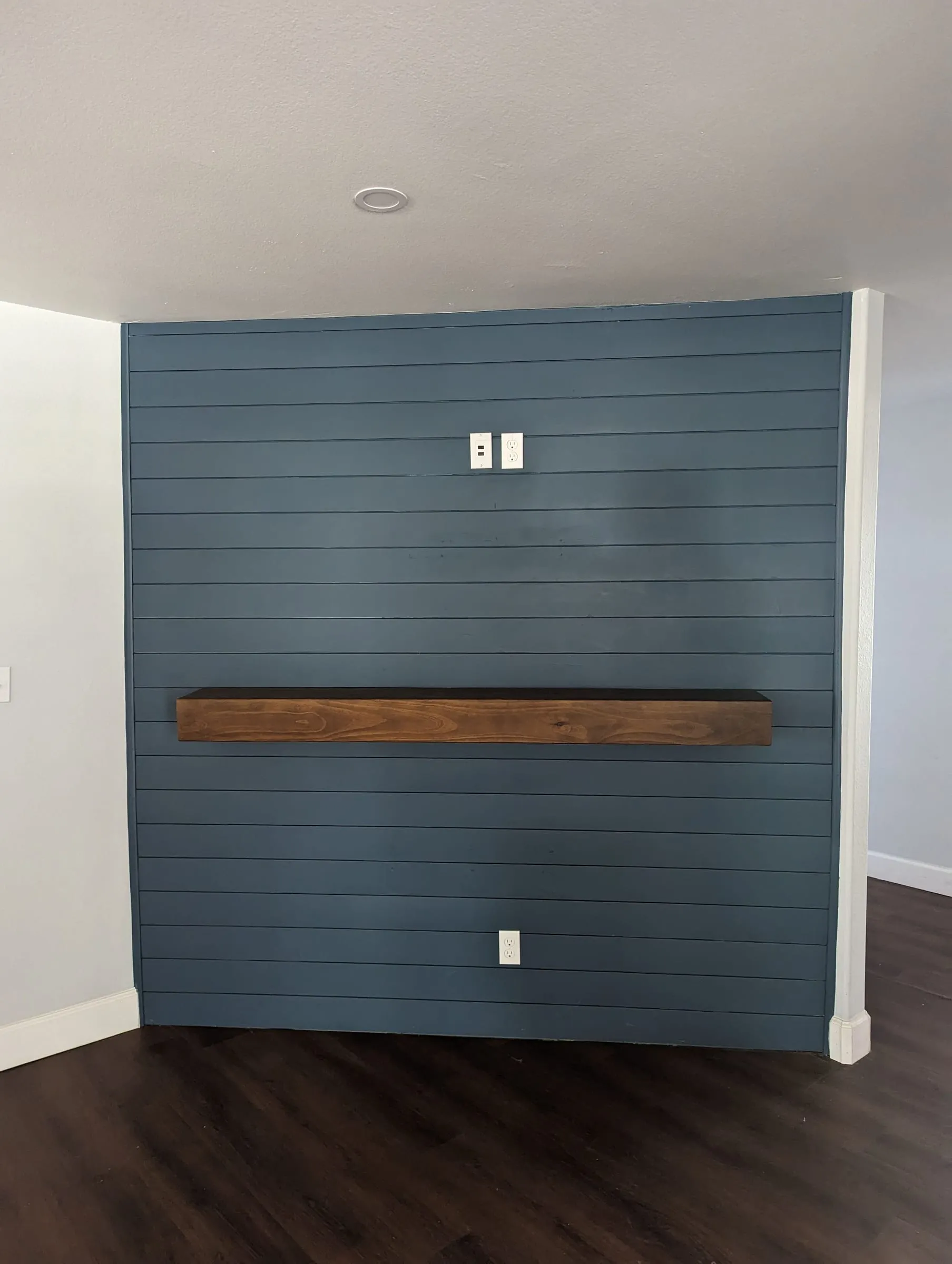Blue shiplap accent wall with a wood mantel over dark plank flooring