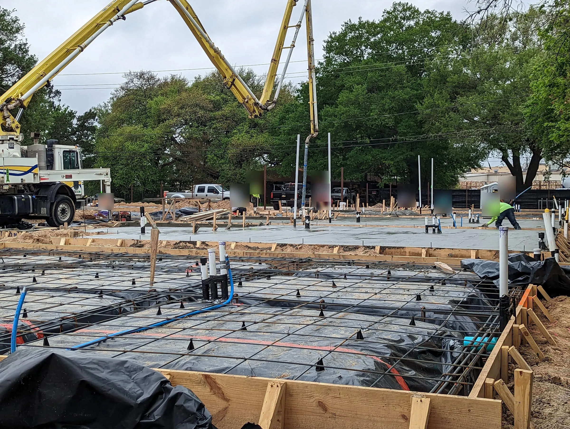 Slab foundation forms with rebar and plumbing stubs while a concrete pump truck works